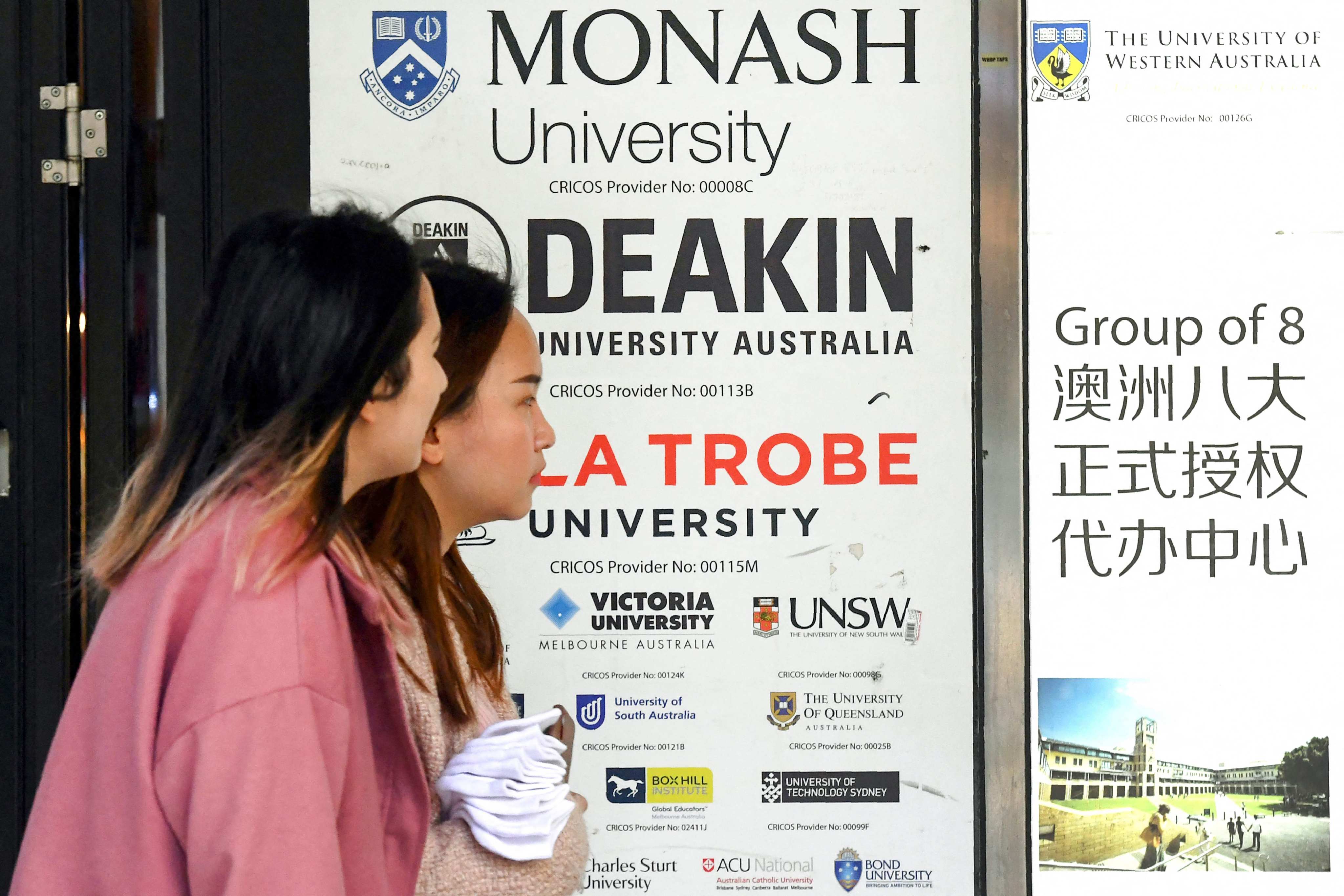 Women walk past signage advertising Australian universities in Melbourne’s central business district. Photo: AFP