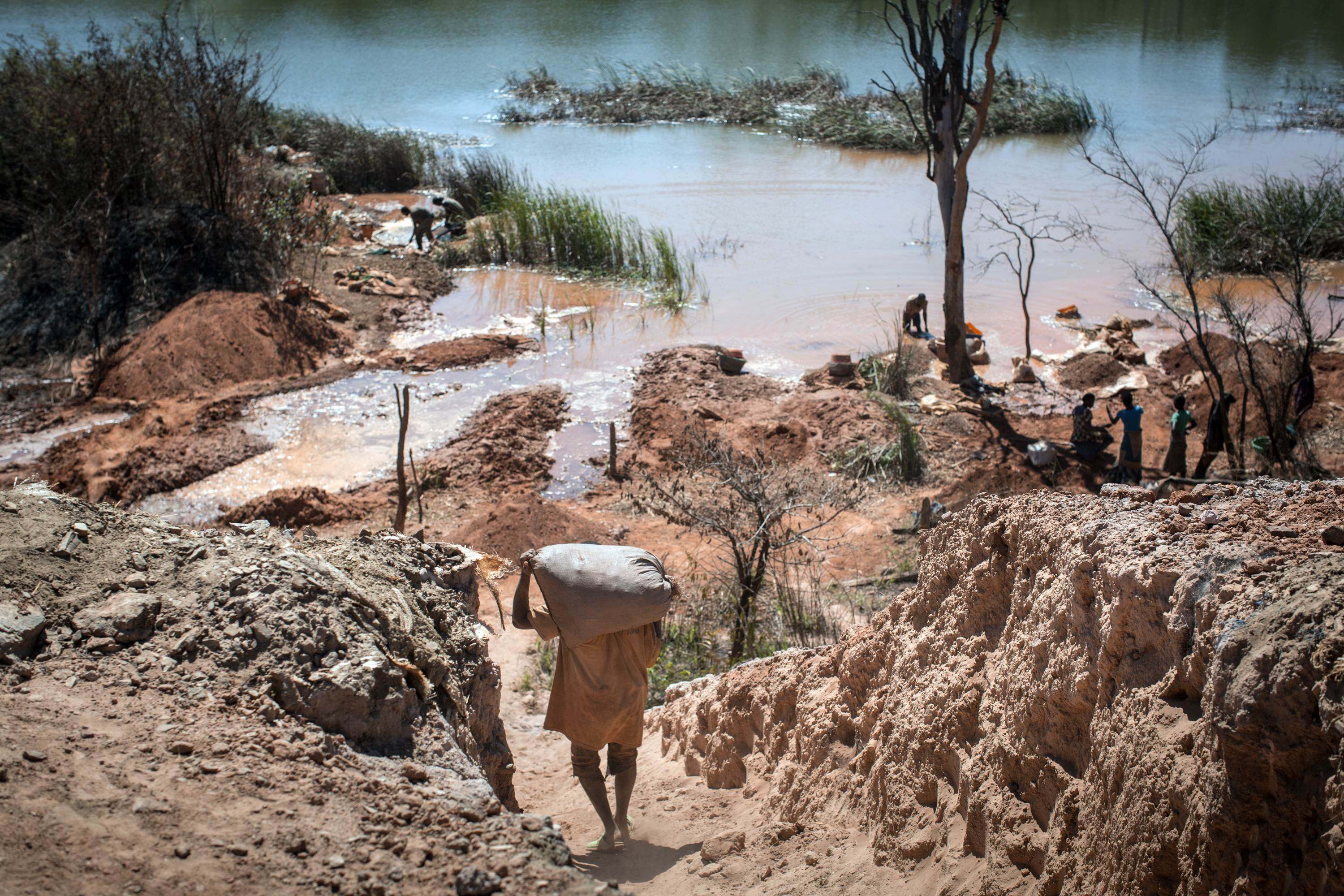 A man carries a bag of minerals as people separate cobalt from sand and rock at a lake near a mine between Lubumbashi and Kolwezi in the Democratic Republic of Congo. Photo: AFP 